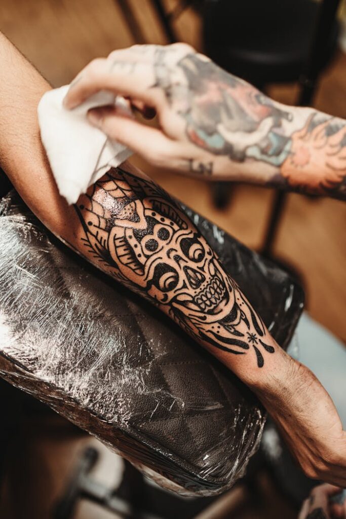 Close-up of a tattoo artist working on an arm with a skull design. Detailed and artistic.
