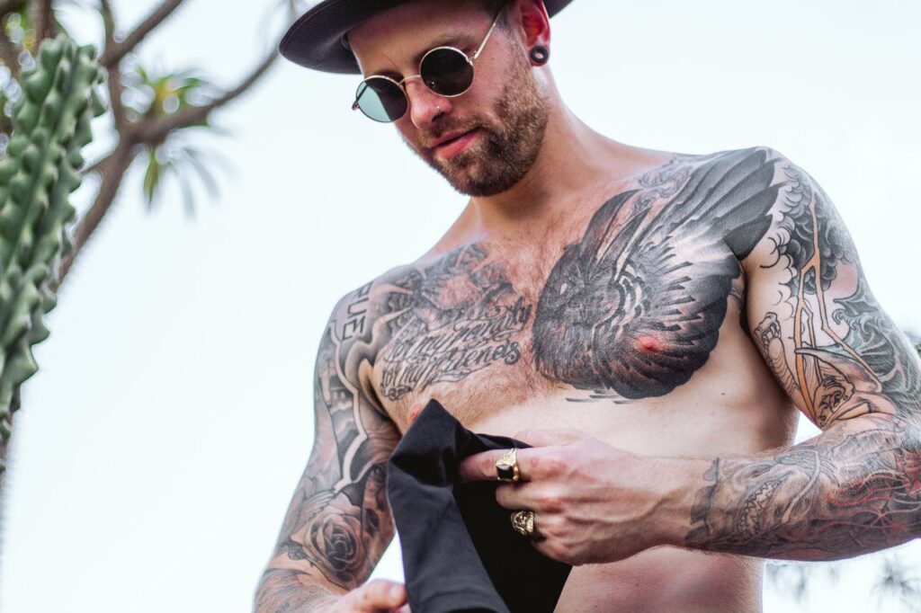 Portrait of a tattooed man in sunglasses and hat outdoors, showcasing intricate body art.