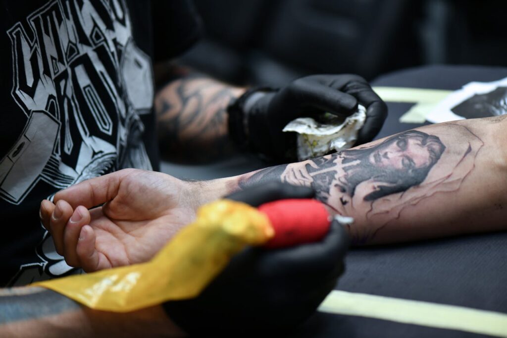 A tattoo artist working on an intricate arm design with tattoo equipment.