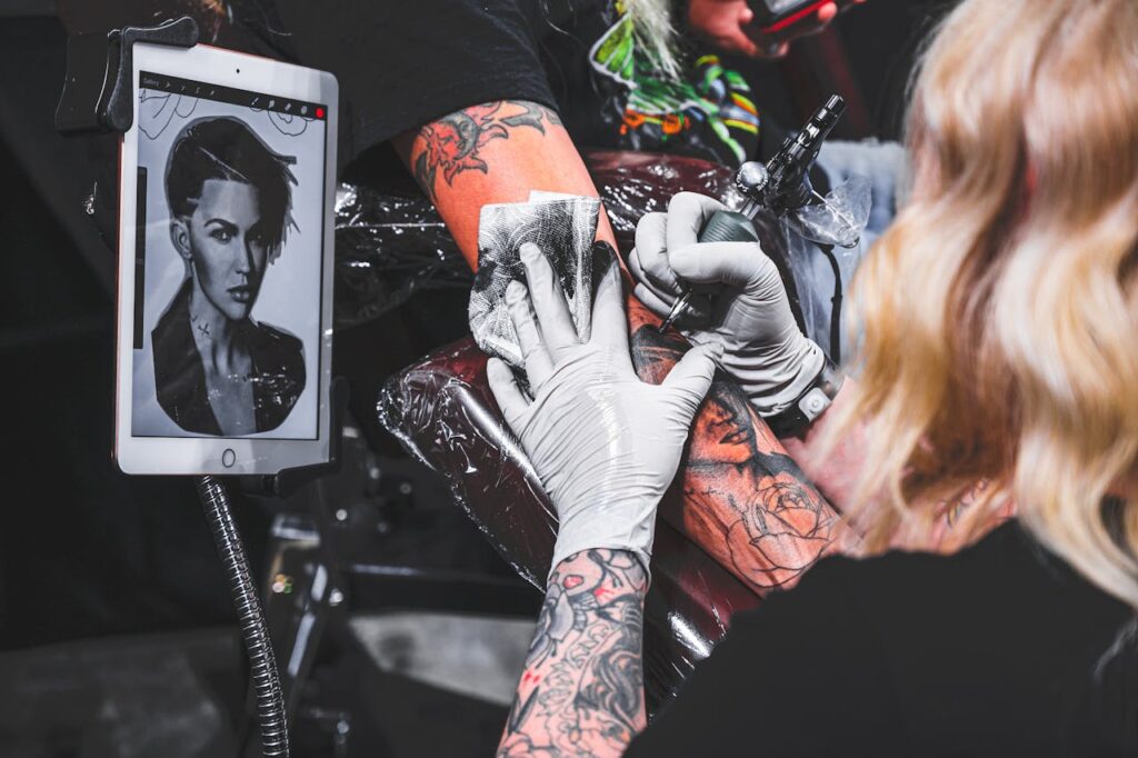 Tattoo artist creating a detailed arm tattoo using modern tools in a studio setting.