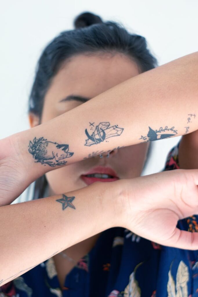 A woman showcasing forearm tattoos with her face partially covered and a nose piercing visible.