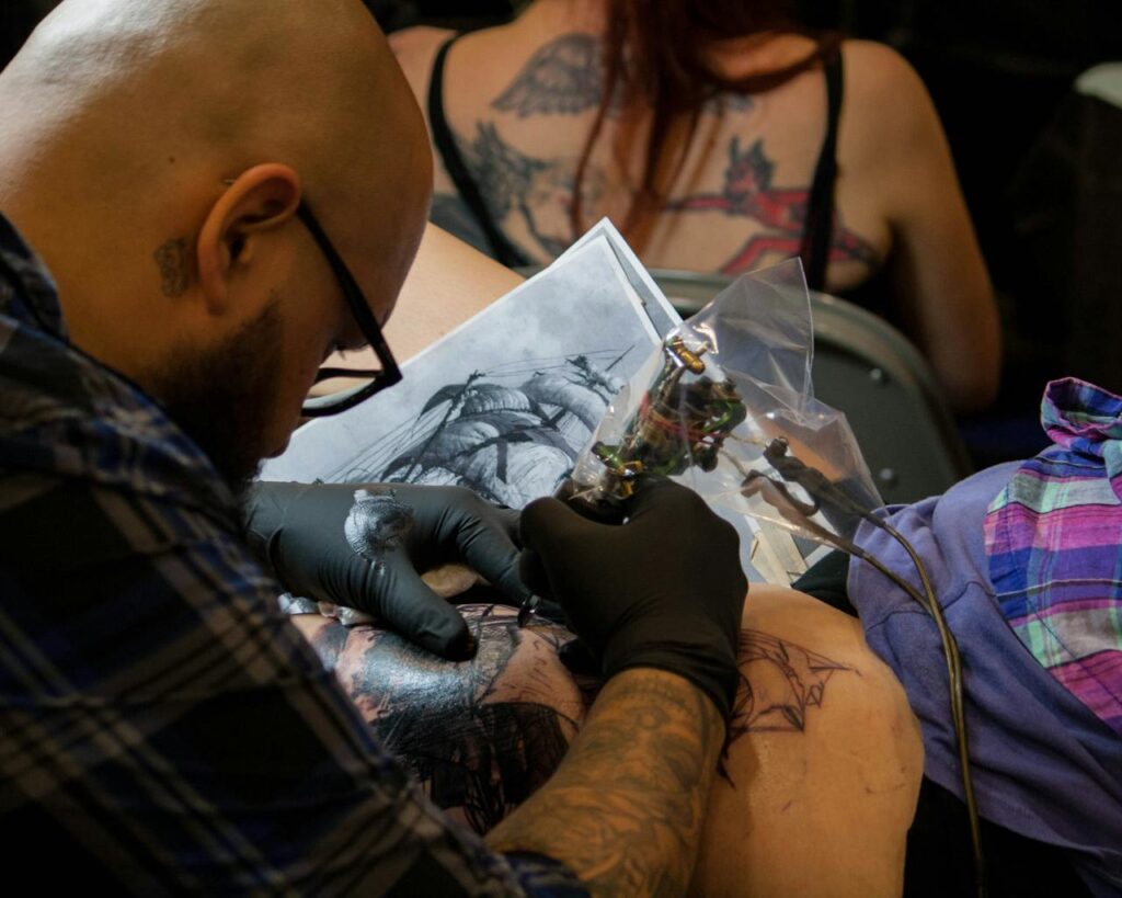 A tattoo artist skillfully works on a detailed arm tattoo in a studio setting.