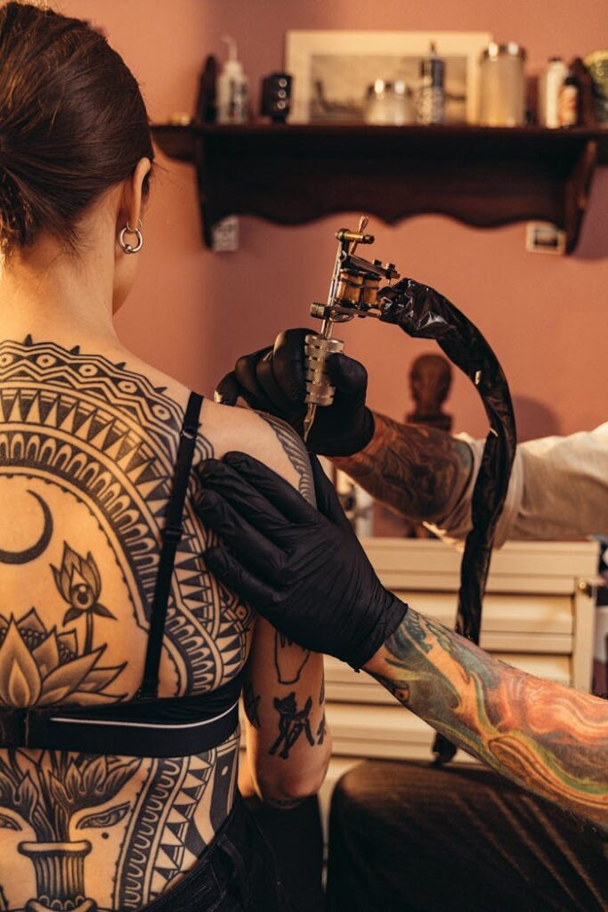 A tattoo artist creates an intricate design on a woman's back in a professional studio.